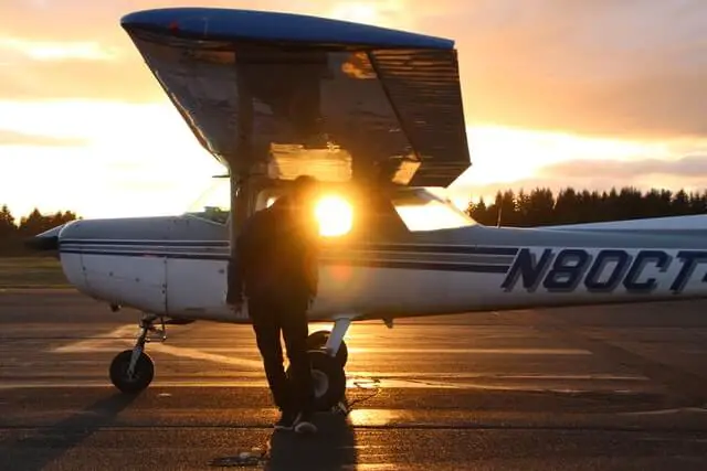 person standing next to small airplane at sunset