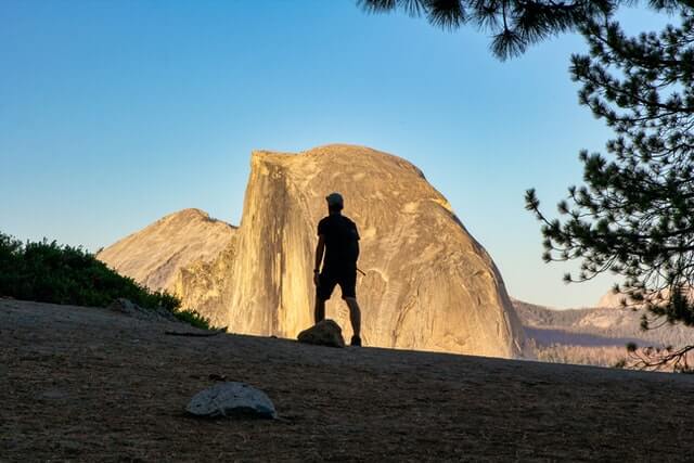 person standing facing a mountain with blue skies