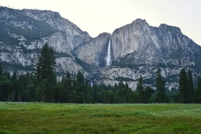 green field with granite peaks and waterfall in the background
