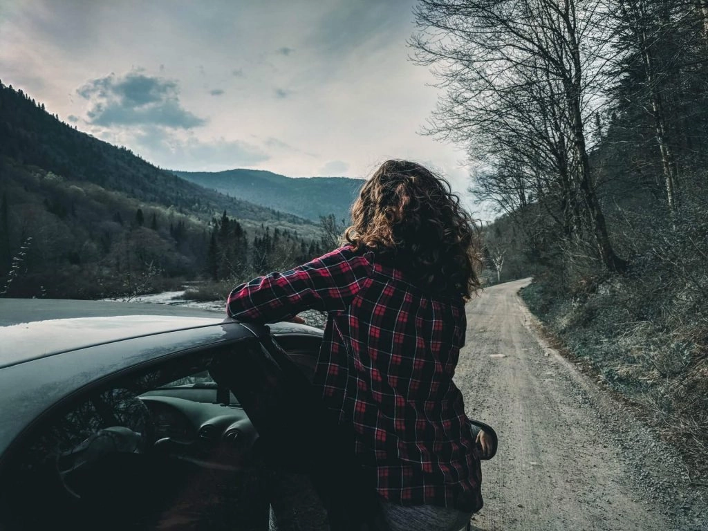 girl leaning out of car window in forest