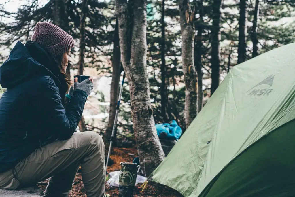 hiker enjoying warm drink by tent