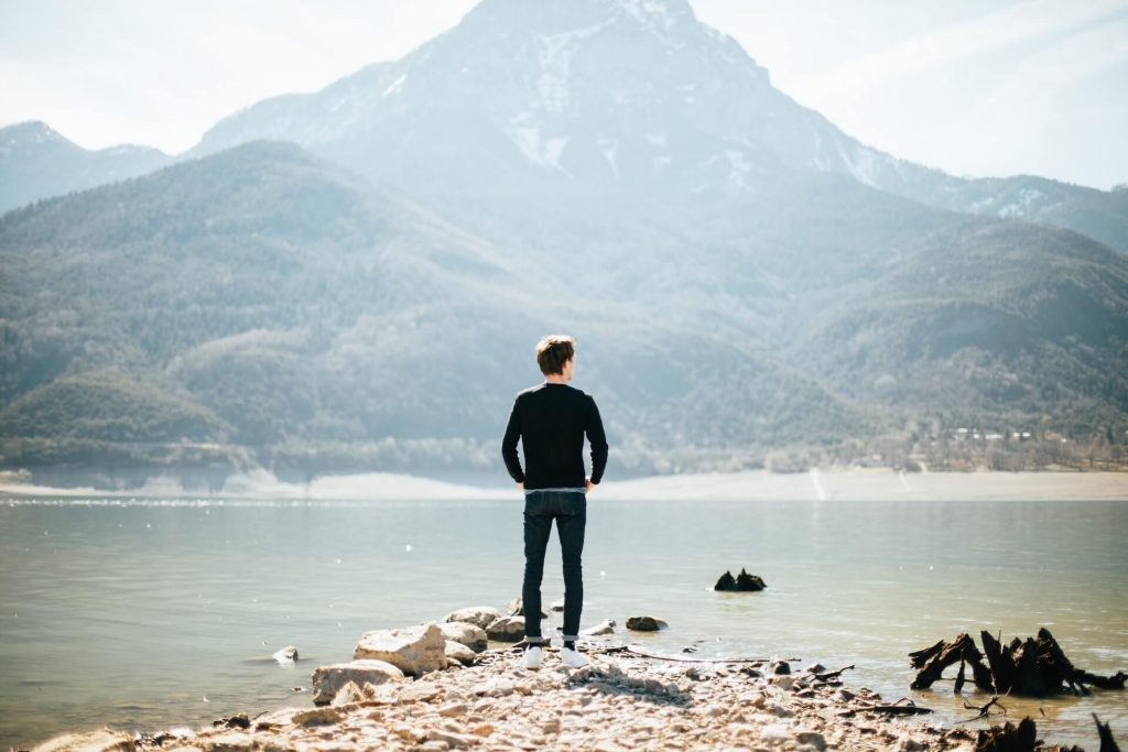hiker in jeans staring at lake and mountain