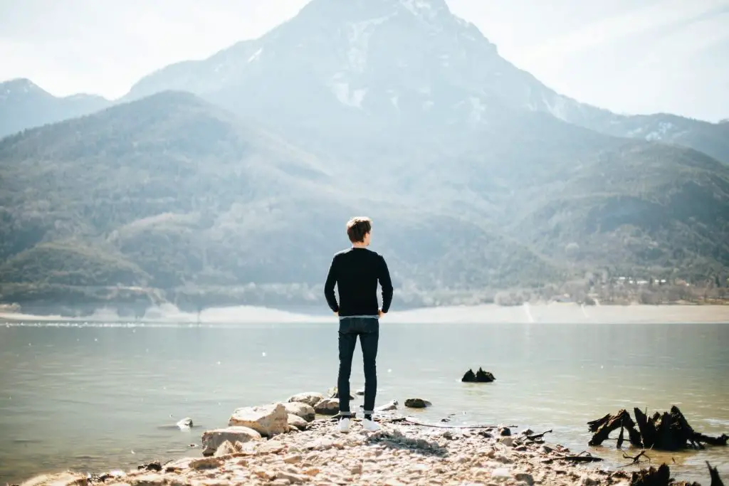 hiker in jeans staring at lake and mountain