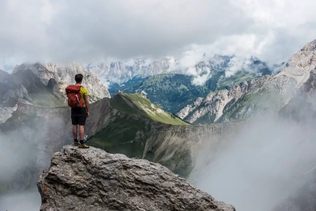 hiker standing on boulder staring at mountain landscape