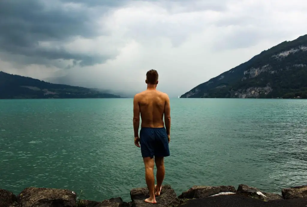 hiker in swim trunks standing by lake