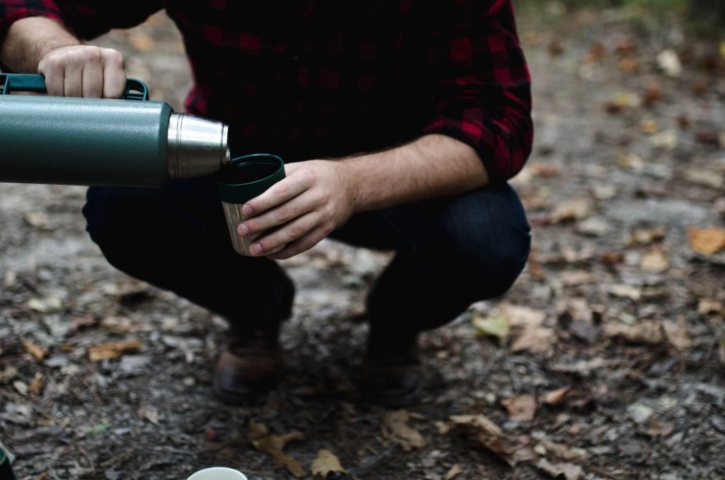 hiker squatting down to pour coffee into cup